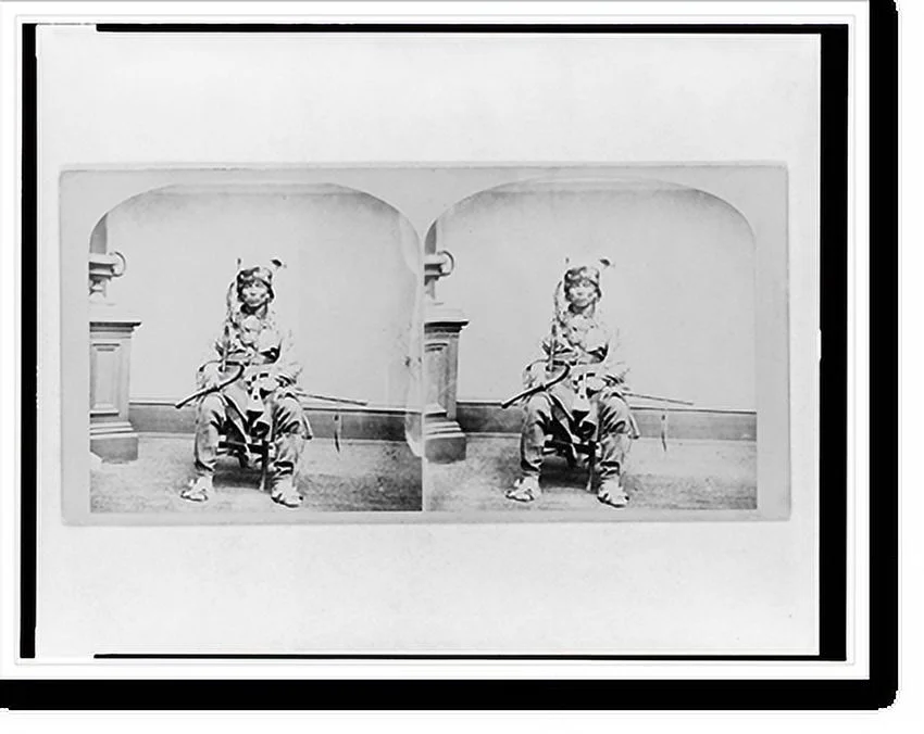 Historic Framed Print, [Winnebago man, full-length portrait, seated, facing front, holding tomahawk and club], 17-7/8" x 21-7/8"